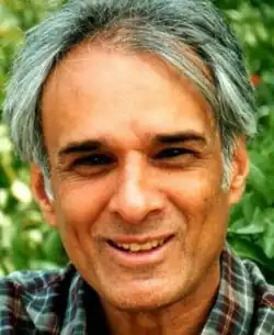 Full-face, colour publicity shot of a smiling, clean-shaven man with grey hair and check shirt