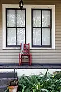 A lonely red chair decorated with Mardi Gras beads sits on a porch.