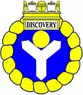 a shakefork—Azure, a shakefork argent supporting in the middle chief a bezant, within an annulet enwreathed, ensigned of a naval crown or, the sails argent, beneath which on a panel argent edged or is the name "Discovery" in letters sable—HM Canadian Ship Discovery