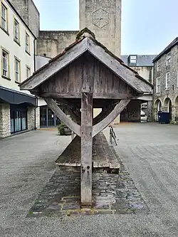Colour photograph of the side of the Shambles. The roof is supported by two trusses and a central oak pillar. The Amulet Theatre, and its hexagon‑shaped, analogue clock, can be seen in the background.