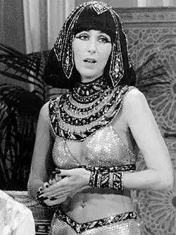 Cher wears an Egyptian-inspired costume featuring an ornate beaded headdress, jeweled collar and a shimmering two-piece outfit with matching bracelets.