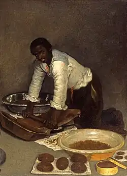 A painting wherein a Black man kneels on the floor, pushing a cylinder into a slab on the floor. Before him are containers with brown powder, and some formed into brown spheres laid out.