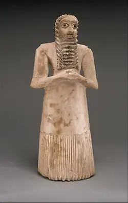Standing male worshiper, one of the twelve statues in the Tell Asmar Hoard; 2900–2600 BC; gypsum alabaster, shell, black limestone and bitumen; 29.5 x 12.9 x 10&nbsp;cm; Metropolitan Museum of Art