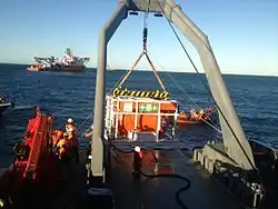 A-frame gantry over the side of a ship with a hyperbaric rescue chamber suspended over the water.