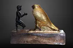 Taharqa offering wine jars to Falcon-god Hemen;[63] 690–664 BC; bronze, greywacke, gold and wood; length: 26&nbsp;cm, height: 19.7&nbsp;cm, width: 10.3&nbsp;cm; Louvre