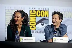 Actors Tawny Newsome and Jack Quaid at a table on stage at Comic-Con in 2019