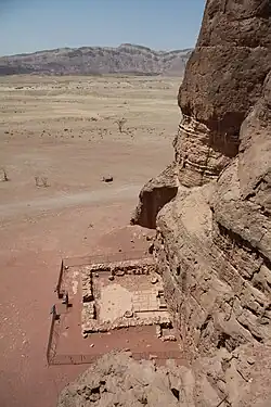 Foundations of a small stone wall at the base of a desert cliff