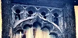 Close up of the top of a second floor window, which is made of old oak wood, cut into an arch with multiple semi circular foils