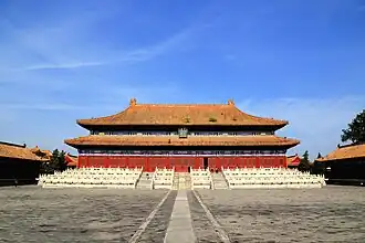 Color photo taken frontally on a sunny day of a stately Chinese-style building with a double roof. The plaque on the building says "Taimiao" ("imperial ancestral temple") in Chinese and in Manchu. The temple is placed on an elevated platform and surrounded by three layers of white fences placed at different heights. Three different flights of stairs lead to the building.
