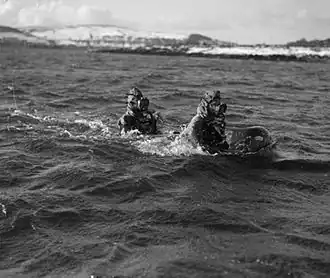 Black and white photograph of two men wearing diving suits with their heads and shoulders just above the water