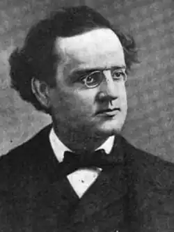 Photographic portrait of a man with spectacles in a bow tie and a formal suit, looking to the right