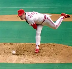 A man in a white baseball uniform with red undersleeves and cap