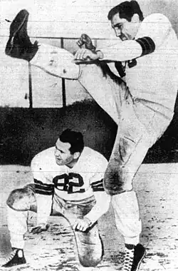 A black and white image of a straight-on American Football placekicker practicing a field goal with a holder
