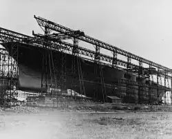 Large ship with no superstructure with scaffold-like steel surrounding her.