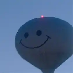 A grainy, blue-tinted photograph of a water tower with a smiley face. A bright red light sits atop the water tower.