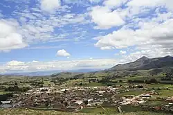 A photo overlooking Tiraque municipality in 2018, during the day with mountains and clouds stretching above the town