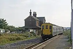 A diesel train with an old station building in the background
