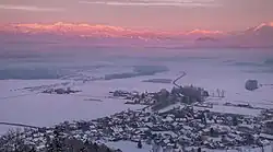 Snow-covered rural town with fields nearby and forests and mountains in the distance