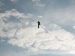 A man walks across a tightrope, with only a clouded sky in the background