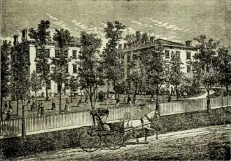 Black and white photo of a school building with trees, a horse and buggy in the foreground