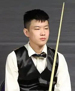Portrait of Zhao Xintong. He is a young Chinese man with short hair, wearing a suit and holding a cue stick.