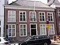 Huis met eenvoudige lijstgevel met kroonlijst op klossen, die overgaan in triglyphen met druppen