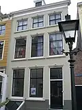 Huis met gepleisterde lijstgevel. Eenvoudige voordeuromlijsting. Dakkapel