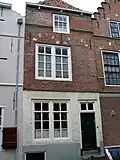 Huis met rechte gevel van rode baksteen. In het metselwerk gele banden en gele blokken in de ontlastingsbogen boven de vensters. Stoeptrapje