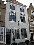Huis met geverfde lijstgevel, aan de hoeken ingezwenkt. Kalf en tandlijst. Stoeptreden