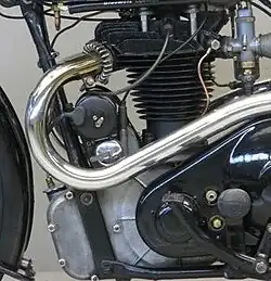 De linkerkant van het motorblok, met de koelribben op de cilinderkop en op de kettingkast (achter het rempedaal) de uitstulping voor de transmissiedemper.