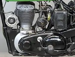 De linkerkant van de motor met links de elektrische claxon, voor op de kettingkast de uitstulping voor de transmissiedemper, achter de cilinder de magdyno en daarachter de accu.