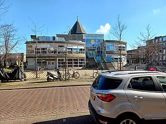 Schoolgebouw midden op het plein met daarachter koepel van de Majellakerk (februari 2022)