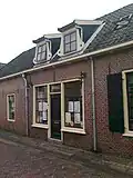 Lage woning onder zadeldak met rechte kroonlijst. Vormt een geheel met de buurnummers 31,35,37