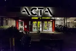 Ingang bij nacht, met felle kleuren die contrasteren met het sobere gebouw (2017)