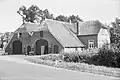 Boerderij met rechts een evenwijdig aangebouwde kortere schuur, beide gedekt door een afgewolfd rieten zadeldak; de beide naar de straat gekeerde en aaneengebouwde achtergevels hebben korfboogvormige toegangen. Links, dwars op de zijgevel van de boerderij, een moderne uitbouw van het woongedeelte