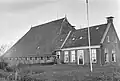 Kop-hals-rompboerderij met voorhuis tussen topgevels met boeiborden, omlijste ingang, zesruitsvensters en topschoorstenen met borden