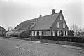 Boerderij van het Langstraatse type, met aan de voorzijde een tuitgevel, bekroond door trappen en een toppilaster. Zesdelige schuiframen en luiken. De stal met afgewolfd rieten dak