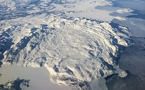 Westwaarts gericht luchtbeeld van het vastelandsgedeelte van de Kiglapait Mountains met linksonder de dichtgevroren Port Manvers. In de linkerbenedenhoek ligt Partridge Point, het noordelijkste punt van South Aulatsivik Island
