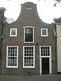 Huis met halsgevel, uitgevoerd in baksteen. Zandstenen voluten