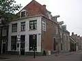 Huis met gepleisterde gevel met rechte kroonlijst, bovenlicht met tonnetjes. Tabakswinkel. Deuren met bovenlicht