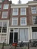 Huis met latere gevel onder rechte lijst waarop een dakkapel in het op het voorste deel van het huis geplaatste dwarse dak