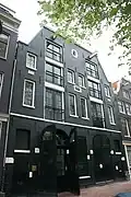 Dubbel pakhuis met dwarse achterbouw en trapeziumgevel waarin stenen met beide jaartallen