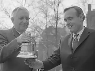 Anthonie Stolk (rechts) luidt de Jacob van Maerlandtklok. Links staat prof. dr. Ph.J. Idenburg die hem de Jacob van Maerlantprijs overhandigt in het ICC gebouw te Amsterdam (19 februari 1964)
