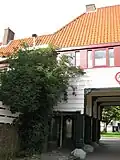 Poortgebouw met twee winkels met bovenwoningen, met veel hout zoals de zware kolommen in poort, bouwstijl Amsterdamse School, ligging aan Purmerweg centraal deel van Tuindorp Nieuwendam