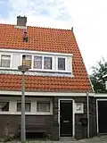 Blok met 8 keukenwoningen, zo genoemd vanwege destijds nieuwe plaatsing van keuken aan de voorzijde, aan de zijkant een houten topgevel, bouwstijl Amsterdamse School, samen met de poortgebouw langs de Purmerweg centraal deel van Tuindorp Nieuwendam