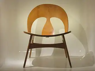 Foto van een stoel gemaakt van licht hout met een ronde rugleuning waarin twee uitsparingen zitten. De foto van de stoel is genomen tegen een witte achtergrond.