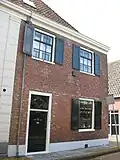 Huis met lijstgevel. Voorgevel grijs gepleisterd. Voordeur met bovenlicht