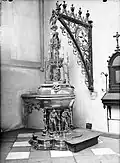 De doopvont uit 1492 door Aert van Tricht, met de zes gebrekkigen als voetstuk en God in de top van de meerledige voorstelling op het deksel.