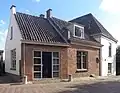 Witgepleisterd huis met verdieping en hoog schilddak, belangrijk door zijn ligging aan de Linge bij de toegang tot het dorp