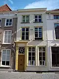 Huis met gebosseerd witgepleisterde lijstgevel, ingang met geblokte pilasters en kroon- en tandlijst en in een cartouche de spreuk: beziet u eerst zelven 1649